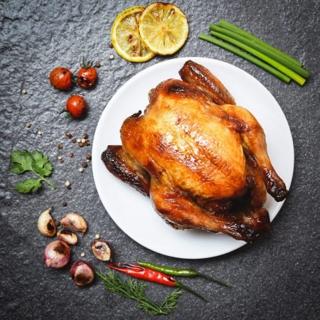 Roasted chicken on plate / baked whole chicken grilled with on herbs and spices and dark background